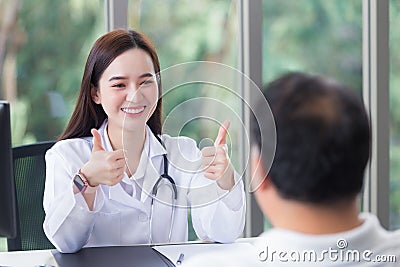 Asian professional woman doctor smiles and shows thump up sign or â€œVery goodâ€ with her patient due to his healthcare at Stock Photo